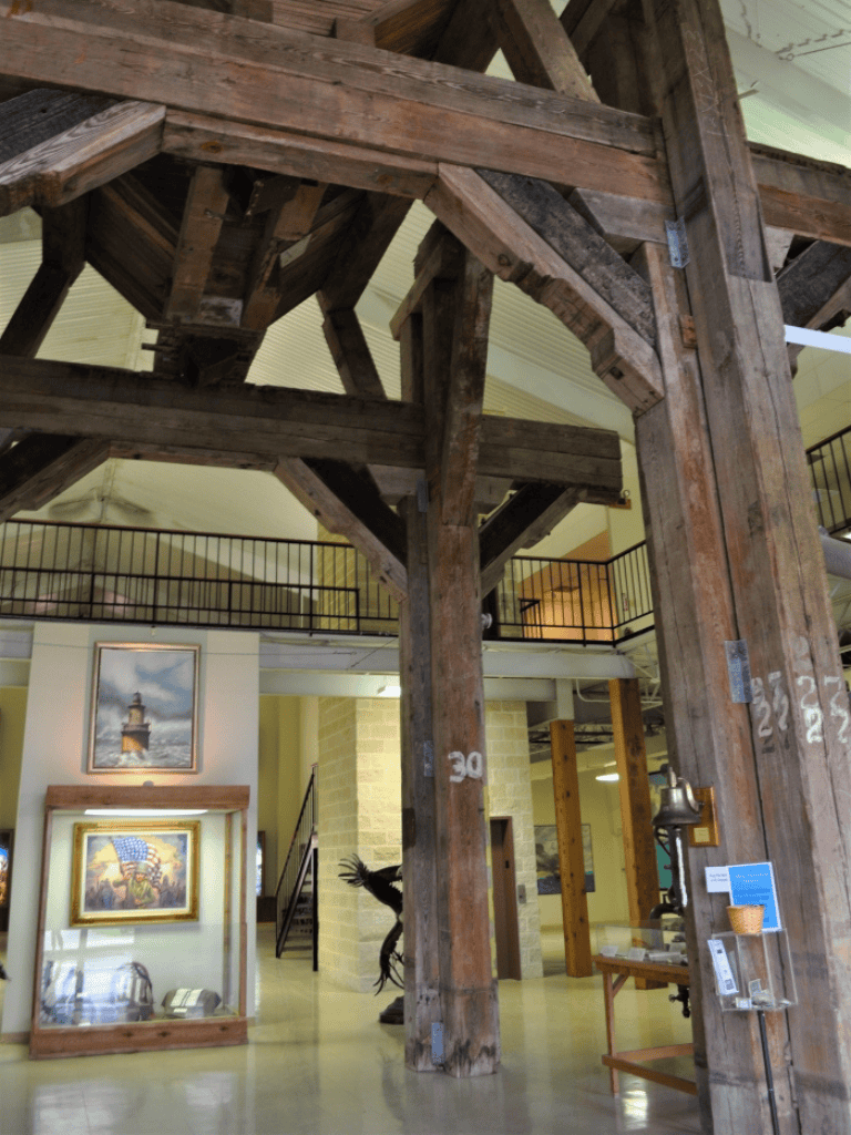 Wooden clock tower structure in indoor museum setting, historical exhibits visible.