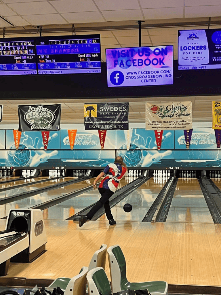 - Bowling alley with player throwing a ball on lane at Crystals Beach, TX, with vibrant digital scoreboards overhead.