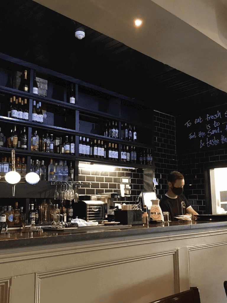 Elegant bar with wine bottles and a bartender wearing a black mask at QuestForDirections.