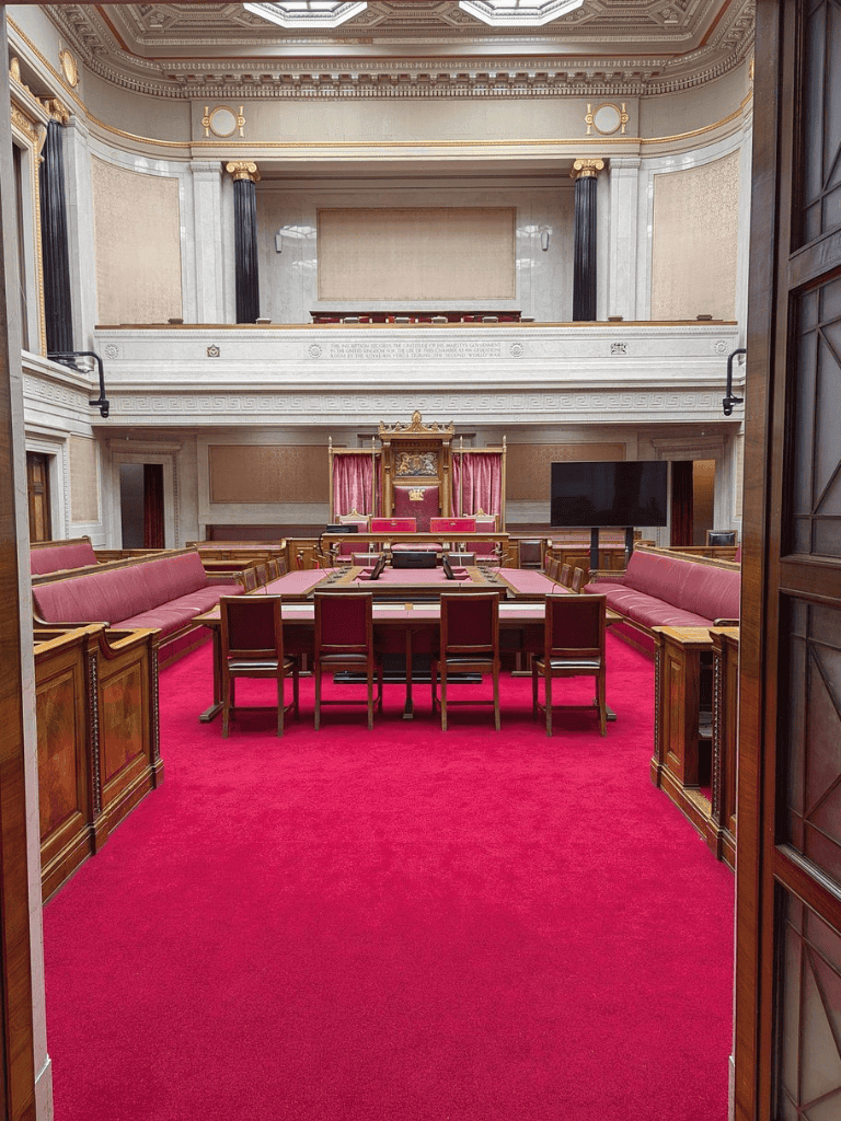 Elegant historic courtroom with wooden furniture and red carpet, featuring a judge's bench and seating area.