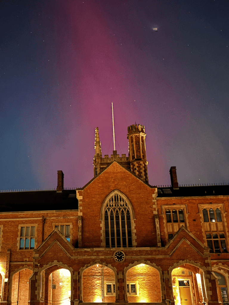 Vibrant night sky with pink aurora over historic brick church with tall spire and gothic windows.