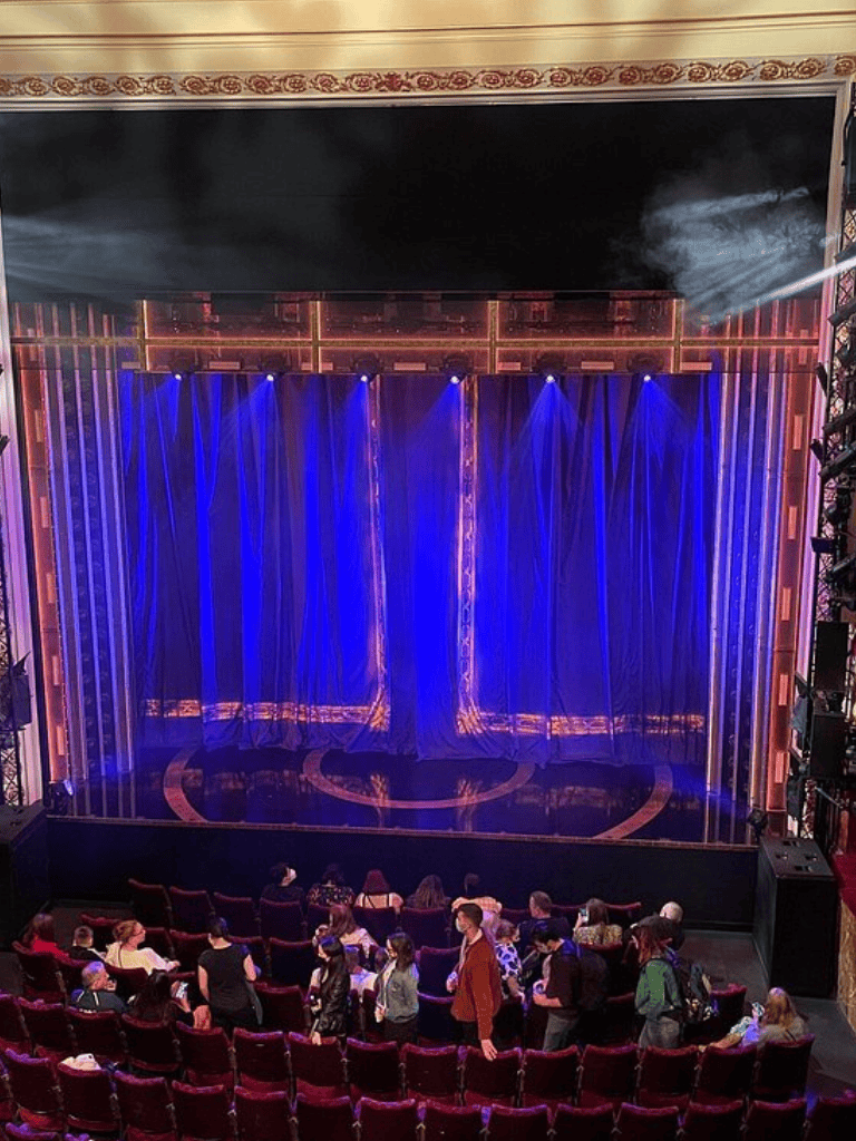 Vibrant theater stage with blue curtains and audience of diverse people waiting for a show.