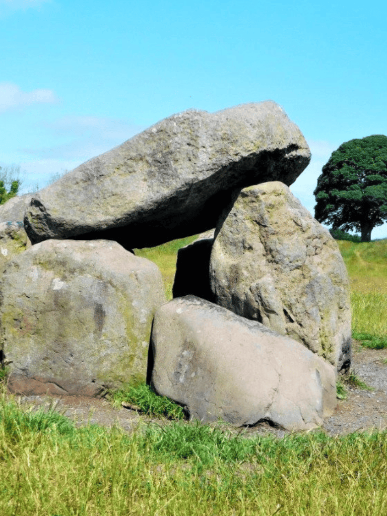 An ancient stone circle with large, balanced rocks on green grass under a blue sky.