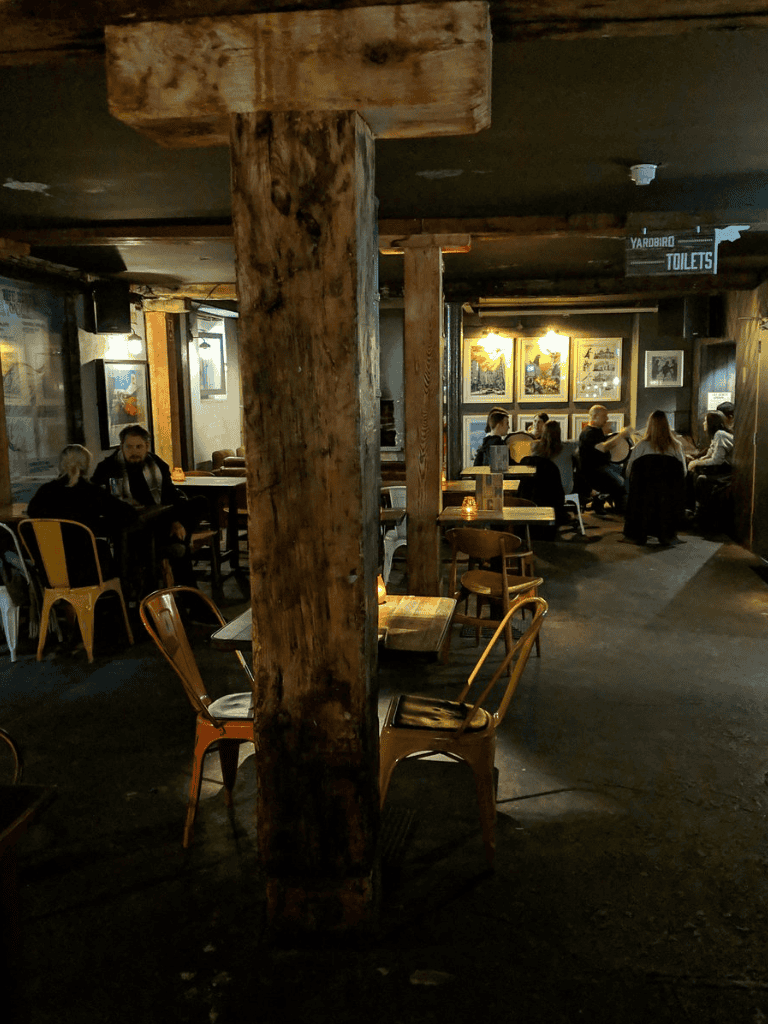 Cozy pub interior with wooden support beams and patrons enjoying drinks and conversations.