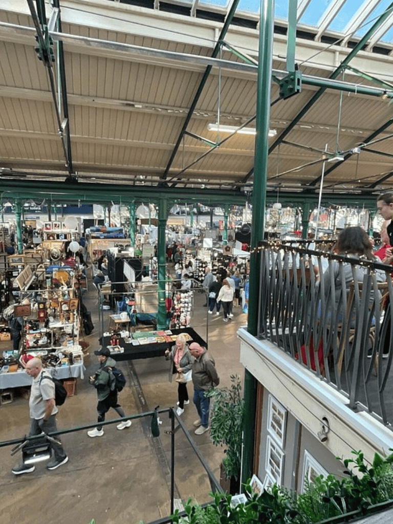 Vintage market with various stalls and shoppers inside a historic building.