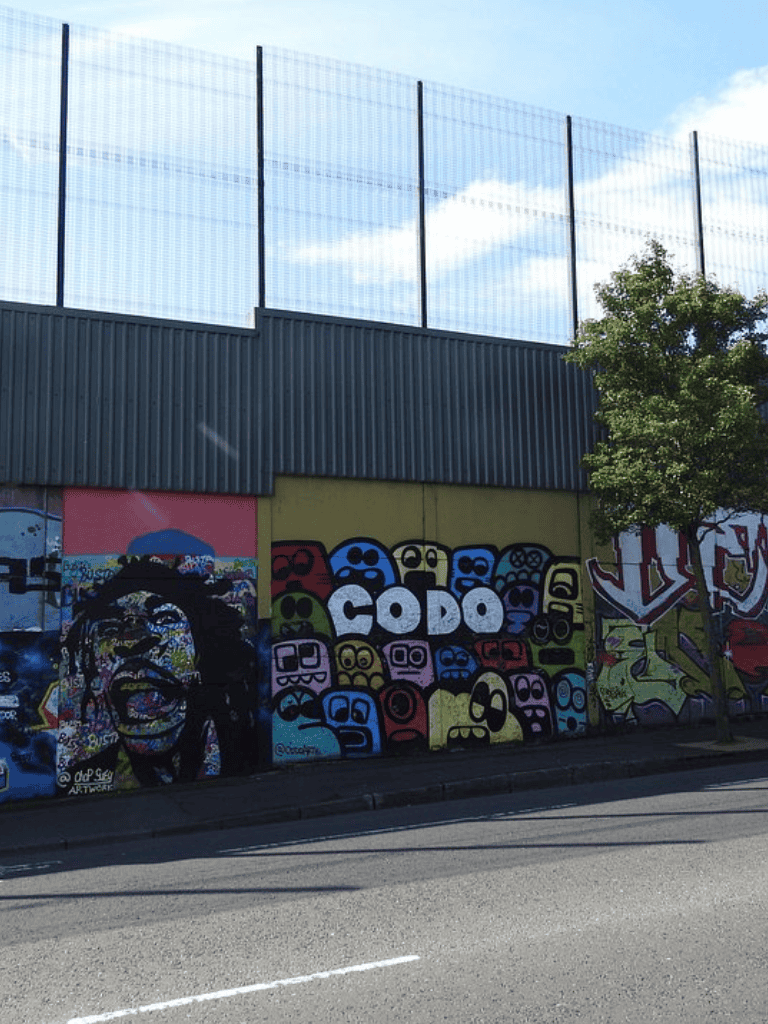 Colorful graffiti art mural with the word "CODO" on a city street wall, featuring vibrant cartoon faces and street art style.