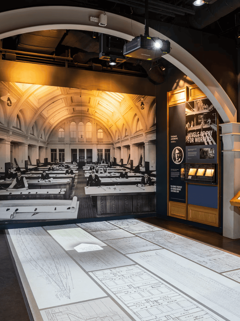 Historic classroom with architectural blueprints on the floor, early 20th-century desk setups, and educational exhibits about work and learning.