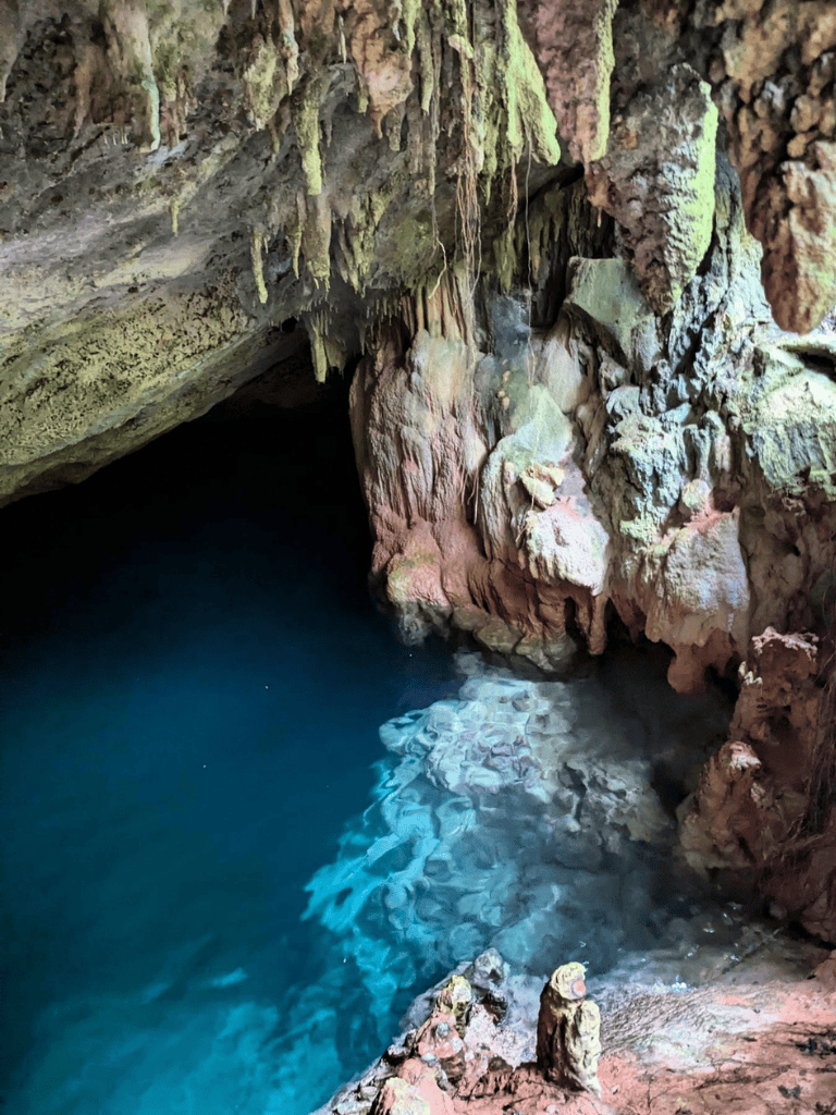Vast underground cave with clear blue water and rugged rock formations.