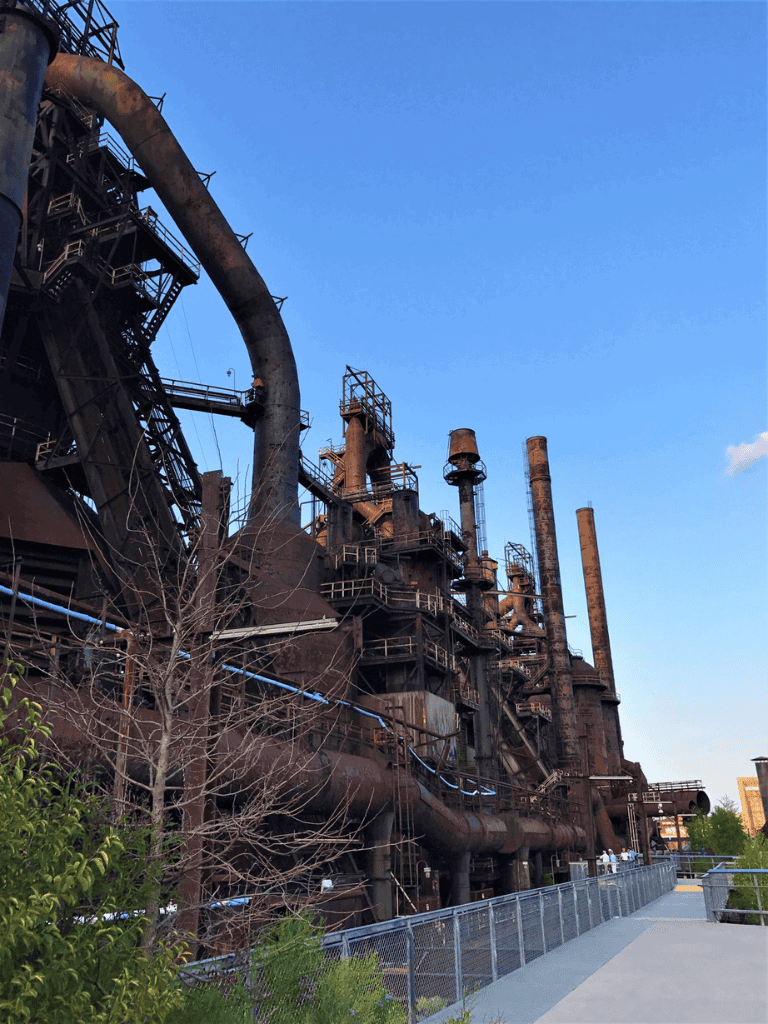 Rusty industrial factory with large pipes and chimneys, against a clear blue sky.