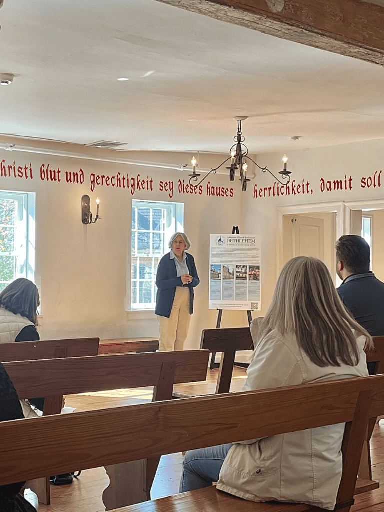 Theologian giving lecture in historic church interior with pews and German inscription on the wall.