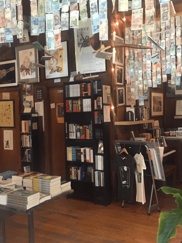 Stacks of international currency notes hanging from the ceiling in a cozy bookstore with bookshelves and framed artwork.