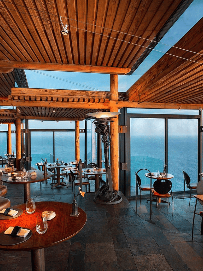 Cozy seaside restaurant featuring wooden ceiling beams and panoramic ocean views, perfect for dining and relaxation.