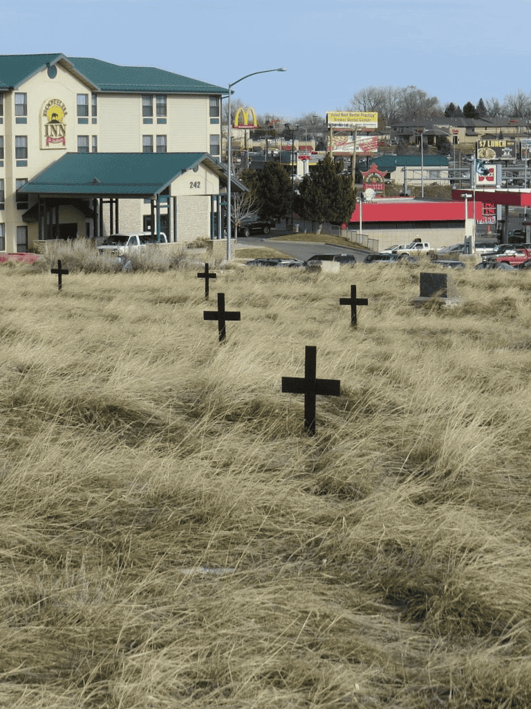 Graveyard with crosses in grassy field in front of commercial buildings and restaurants.