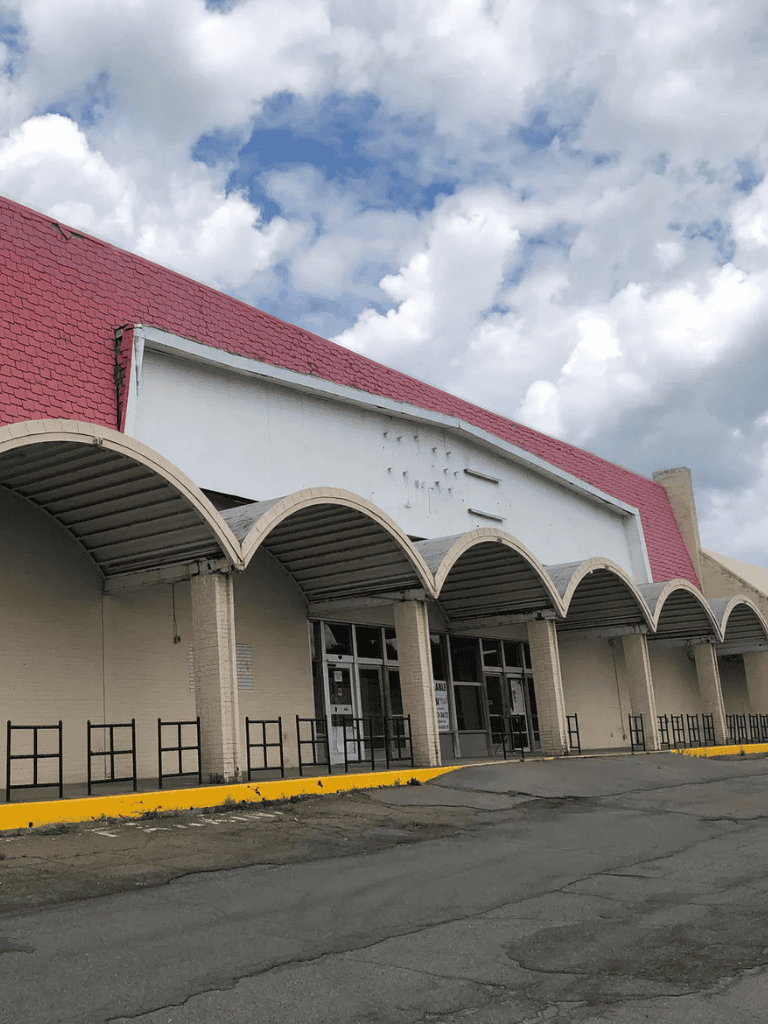 Abandoned retail store with distinctive curved awnings and red roof, located in a commercial area.