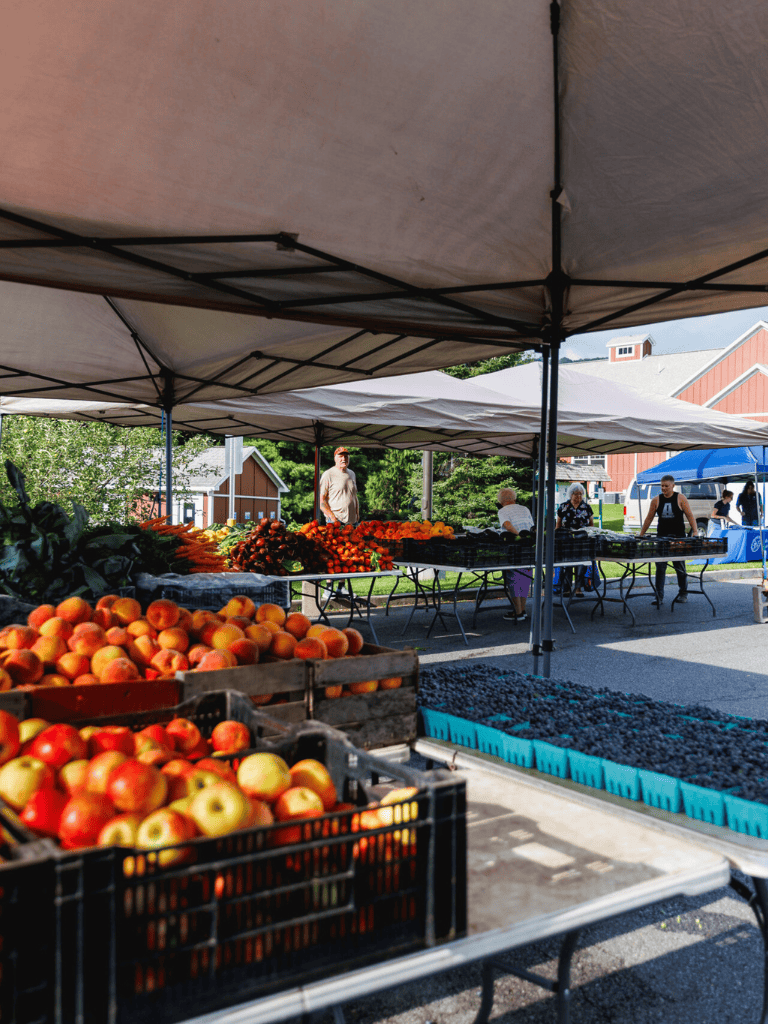 Fresh local produce at a farmers market under tents, showcasing apples, berries, and vegetables.