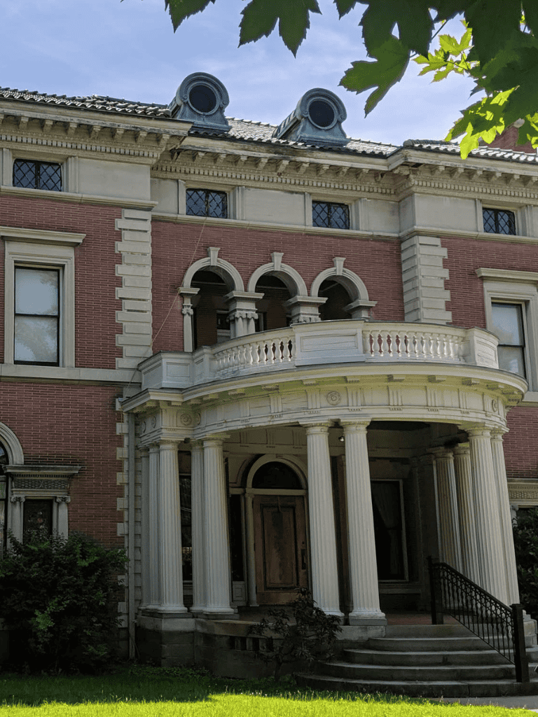Elegant historic mansion with grand porch and classical columns, located in a lush green setting.
