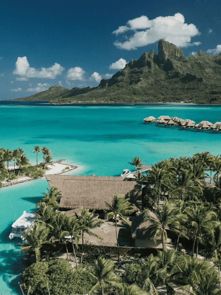 Pristine tropical island with overwater bungalows and lush palm trees, set against a stunning mountain backdrop.