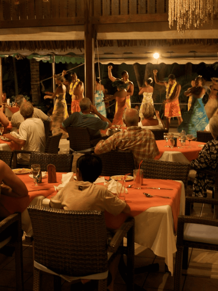 Vibrant Polynesian dance performance at a tropical resort restaurant at night, lively entertainment for guests.