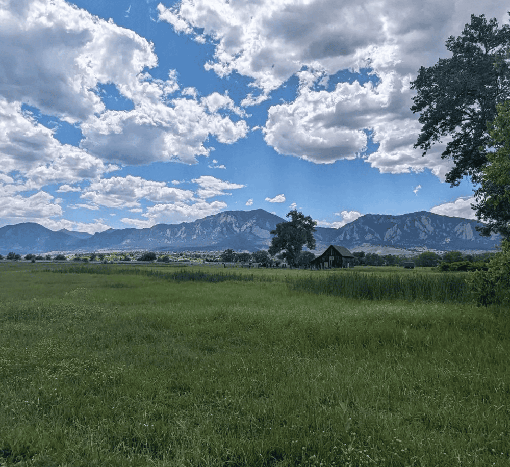Wide open rural field with mountains in the background, blue sky, and scattered clouds, perfect for scenic nature exploration.