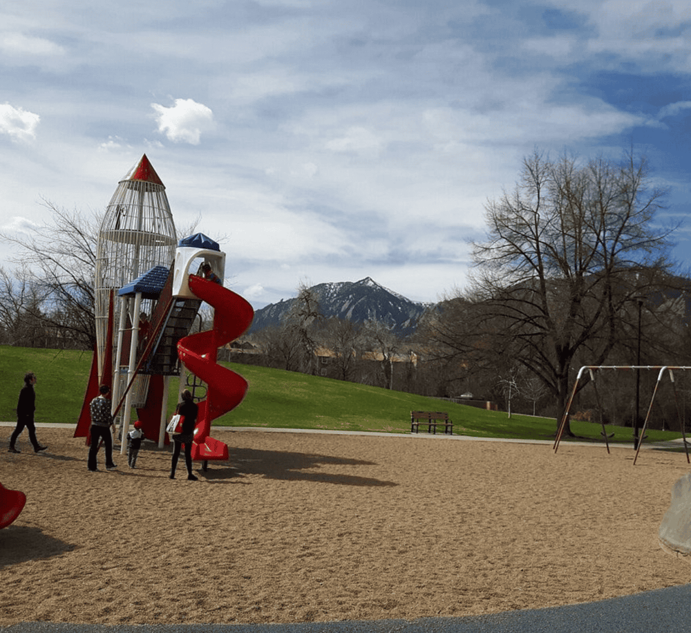 Colorful playground with slide and climbing structure in mountain park setting.