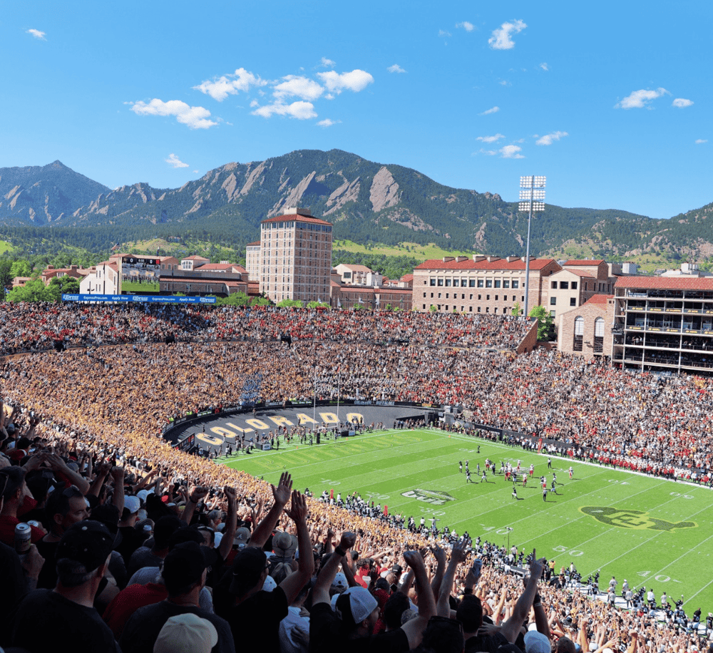 Crowd attending Colorado Buffaloes football game at Folsom Field with scenic mountain backdrop.