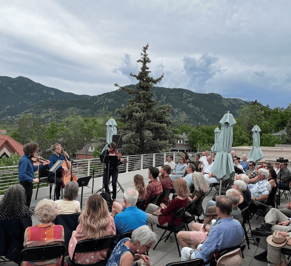 Outdoor musical concert with string quartet overlooking mountainous landscape during daytime.