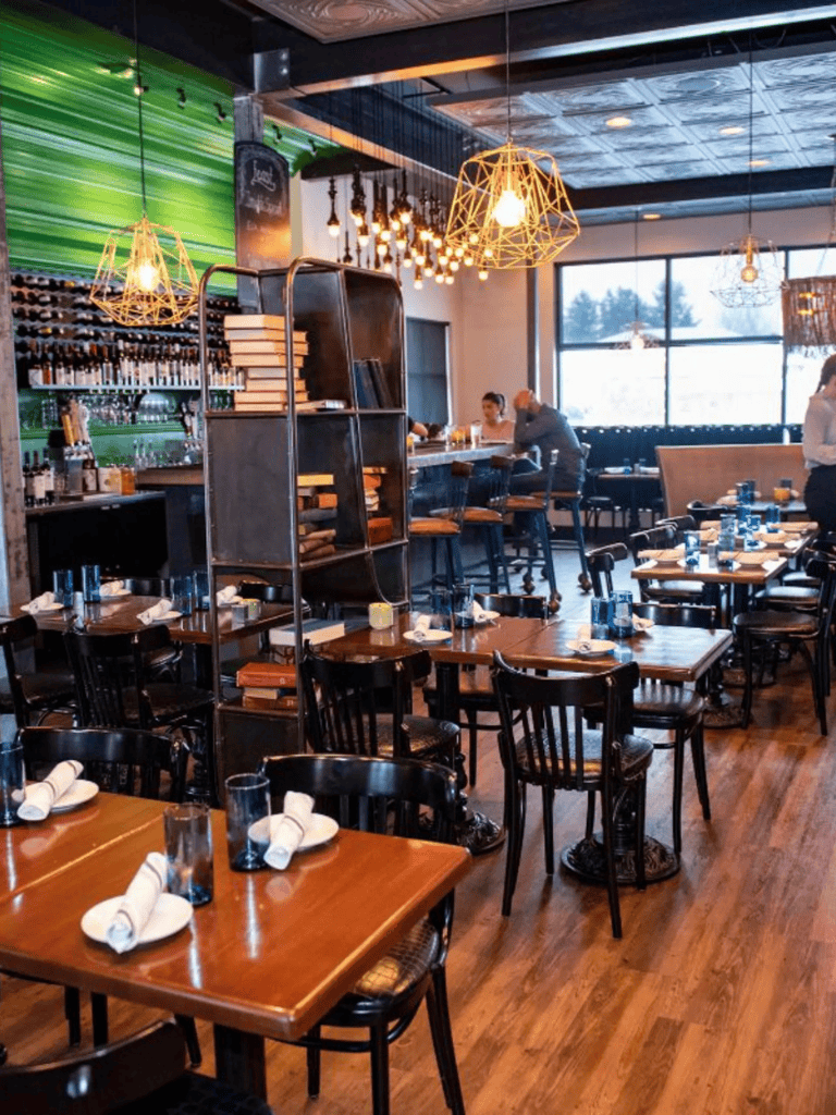 Cozy modern restaurant interior with wooden tables, black chairs, and decorative lighting.