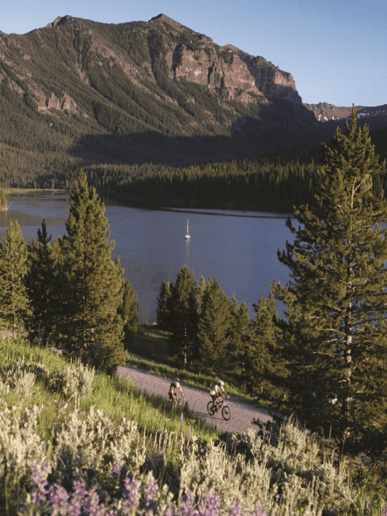 Tranquil mountain lake with cyclists biking along scenic trail amidst lush forests.