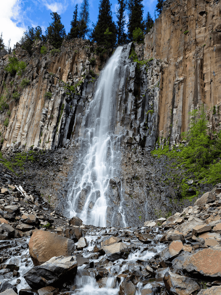 Majestic waterfall cascading down rugged cliffside in a lush forest setting.