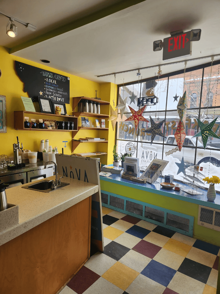 Bright yellow cafe interior with colorful checkered floor and star decorations on large window.