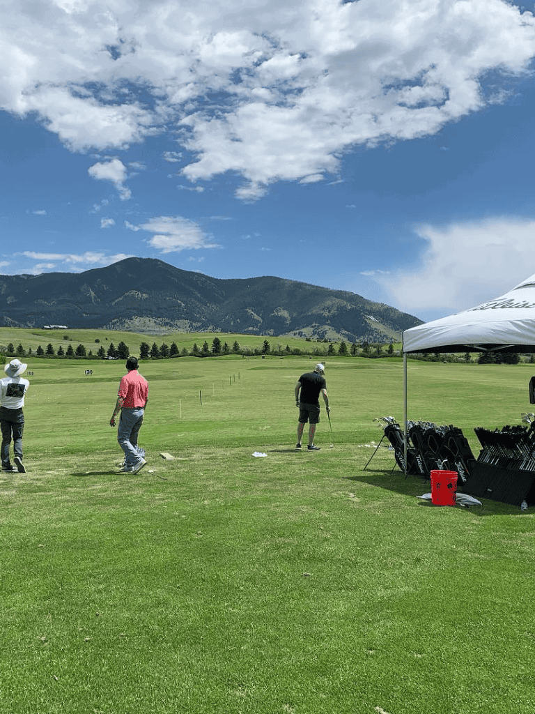 Aerial view of golf practice range on a sunny day with mountains in background.