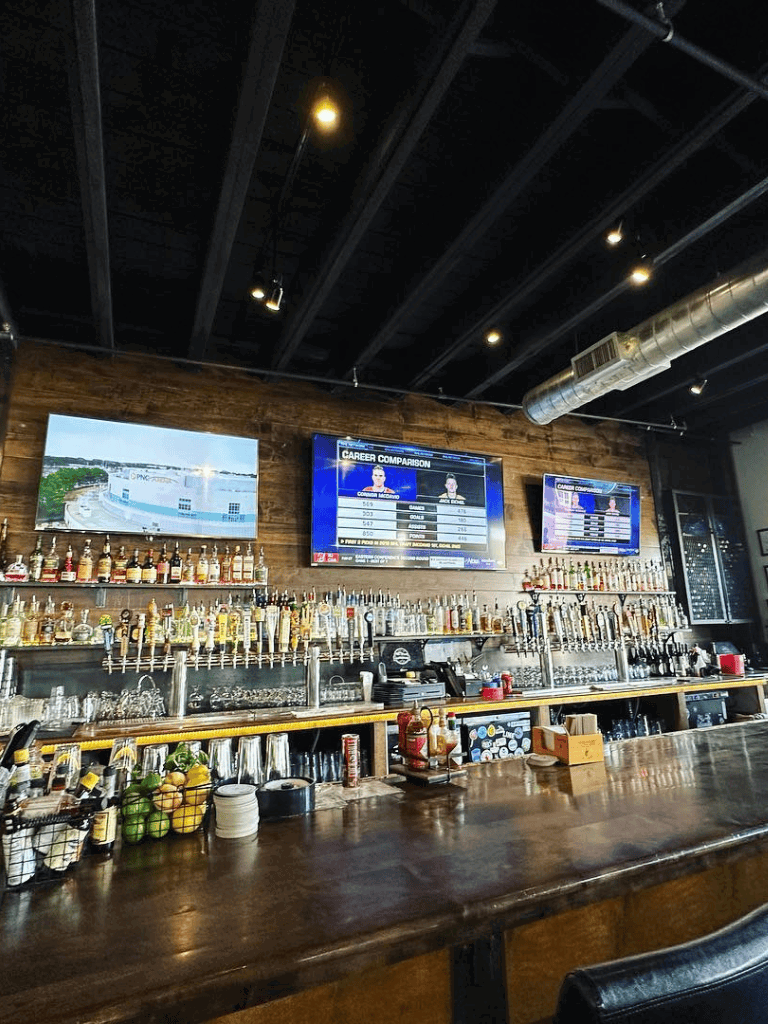 A bar with multiple liquor taps and TV screens displaying sports and career comparison graphics.