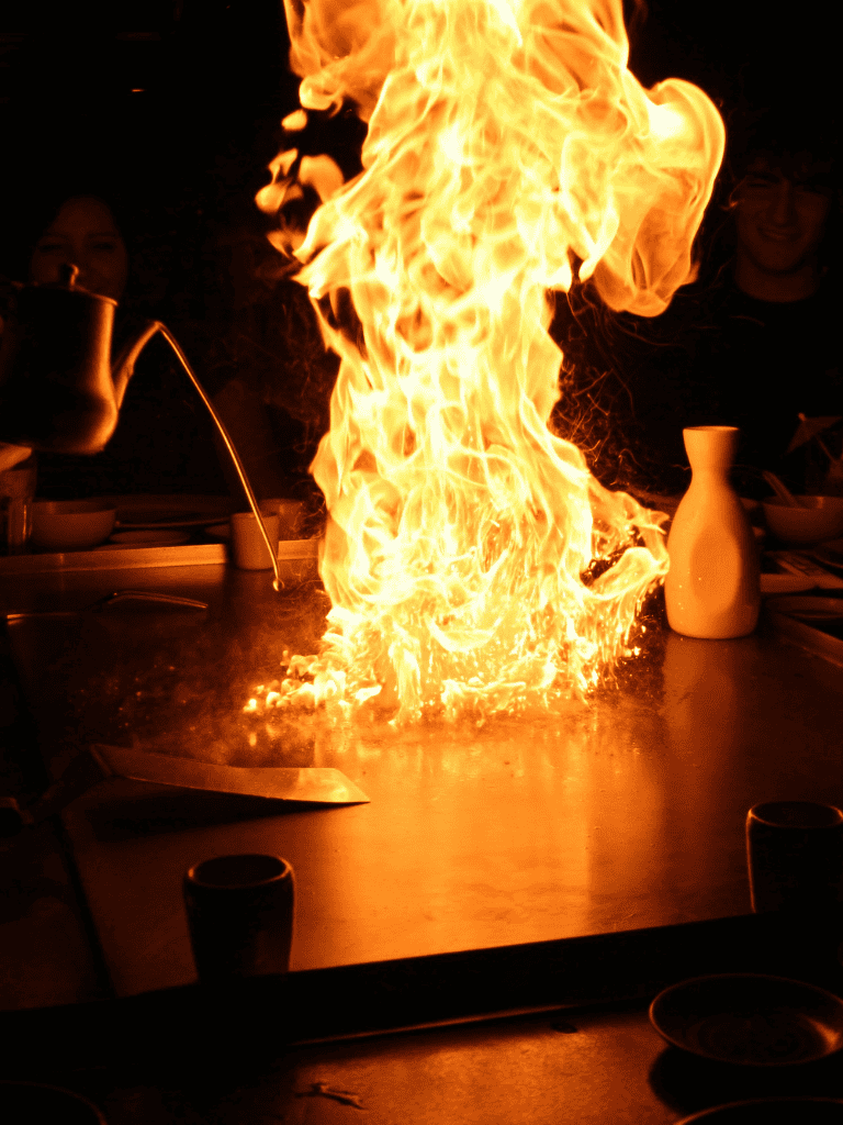 Vibrant flames fill the air during a teppanyaki cooking show at a dinner table.