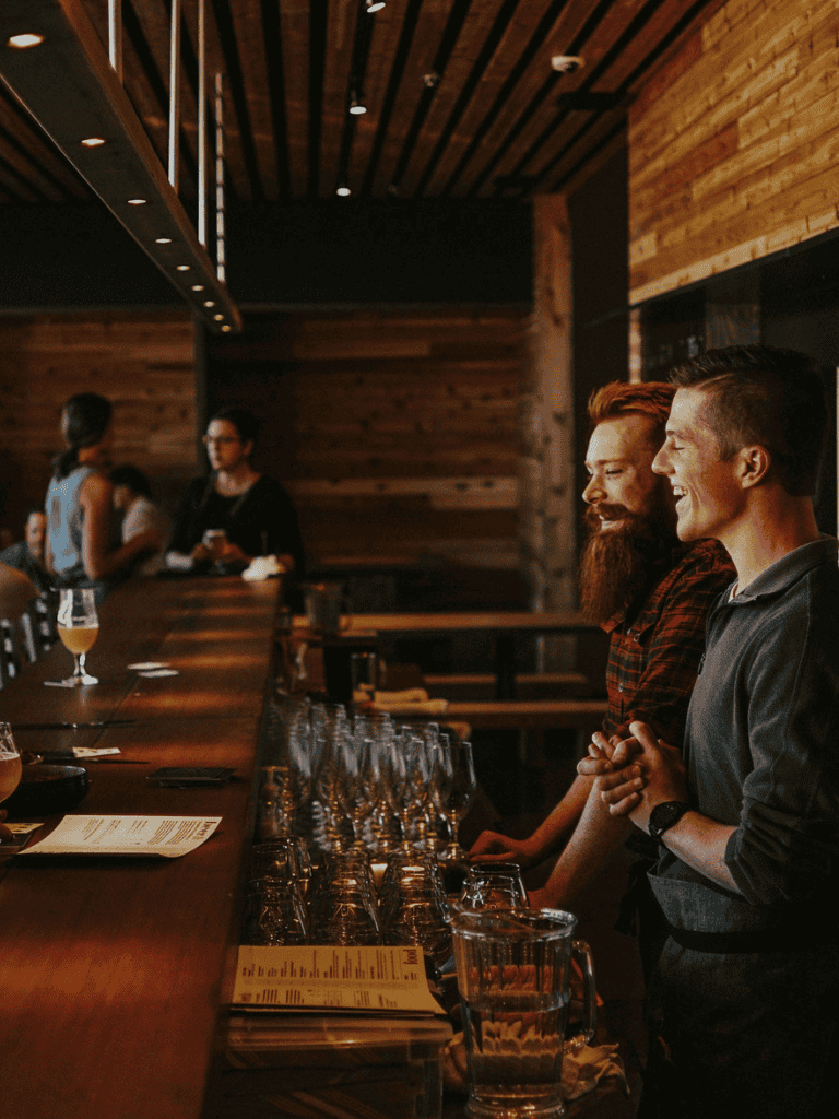 Friendly bartenders chatting at a cozy bar with craft beers and warm wooden interior.