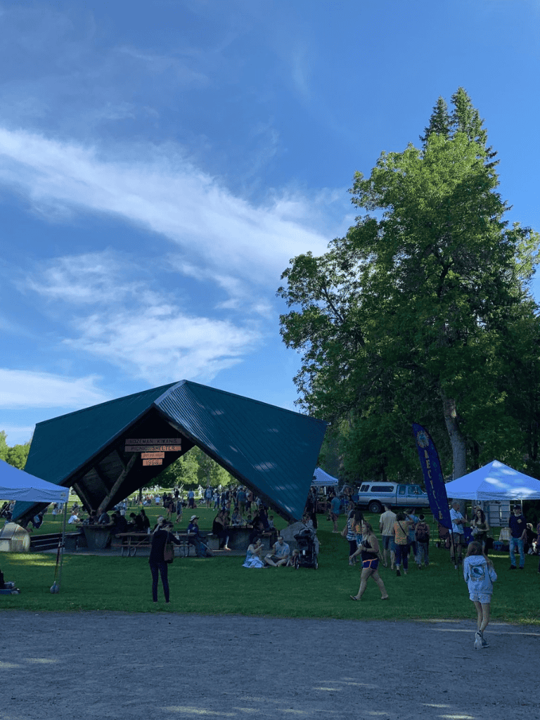 Open-air community event with tents, a pavilion, and people enjoying a sunny day outdoors.