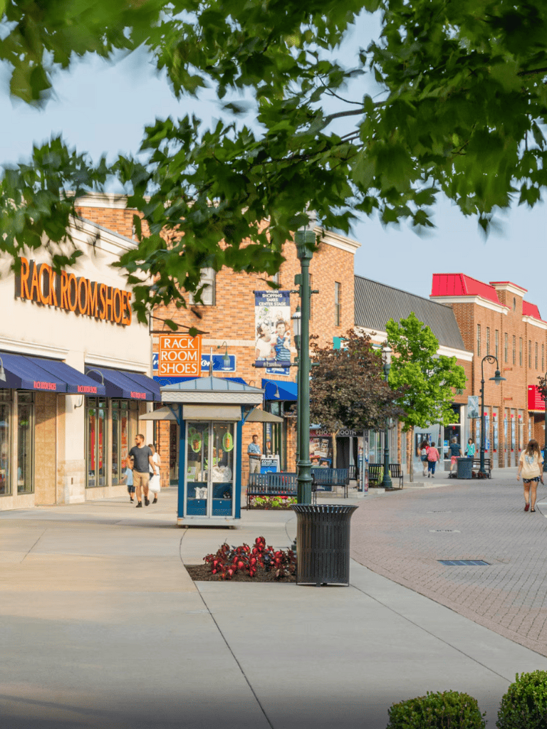 Outdoor shopping plaza with retail stores, seating areas, and pedestrians.