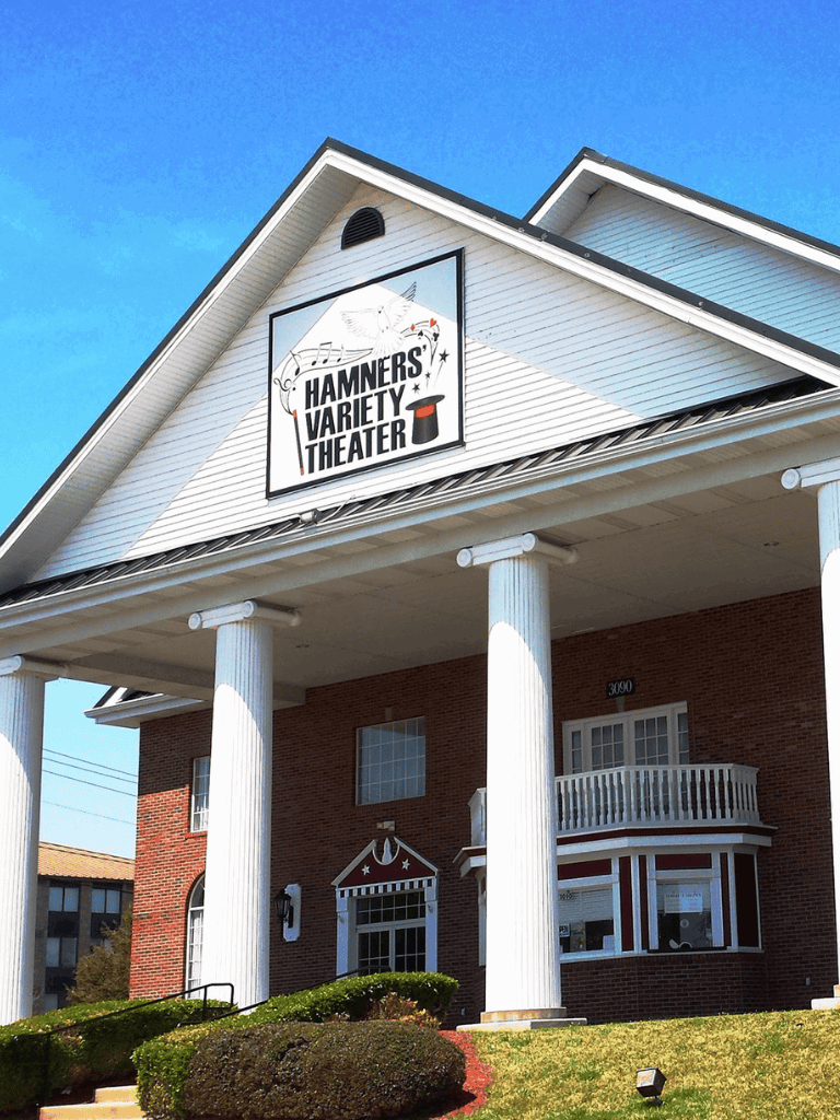 Charming theater with white columns and a colorful sign for Hamner's Variety Theater under a clear blue sky.