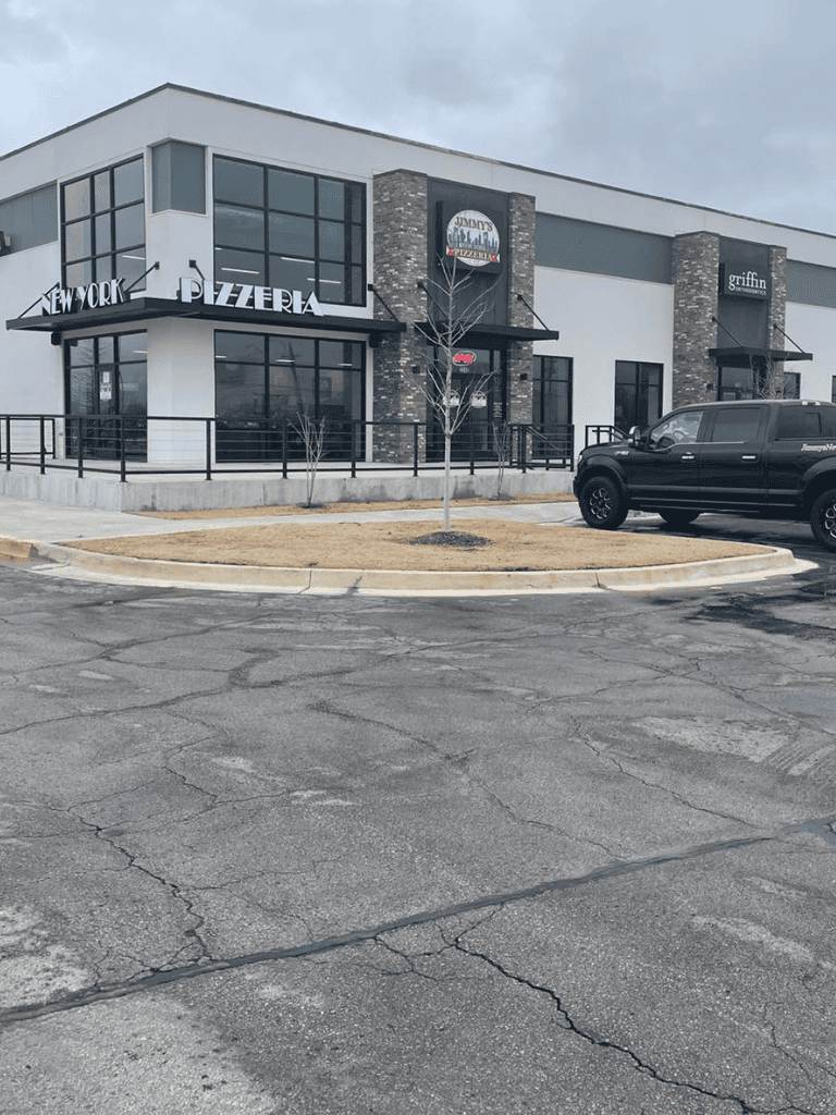 Modern pizzeria and restaurant exterior with large glass windows and parking lot in front.