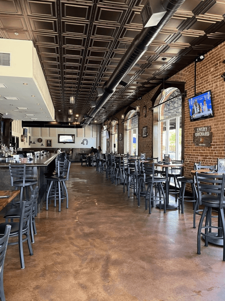 Empty restaurant interior with brick walls, wooden floors, and large windows for a modern dining experience.