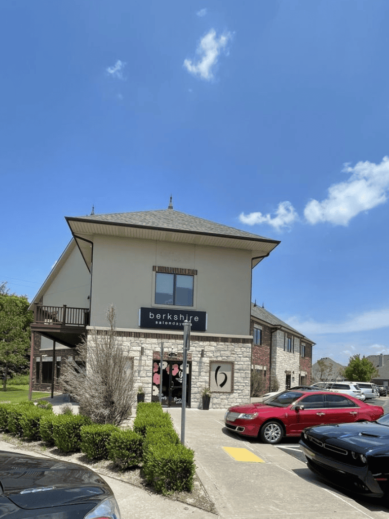Elegant salon exterior with modern architecture, lush greenery, and parking lot, perfect for beauty and wellness services.
