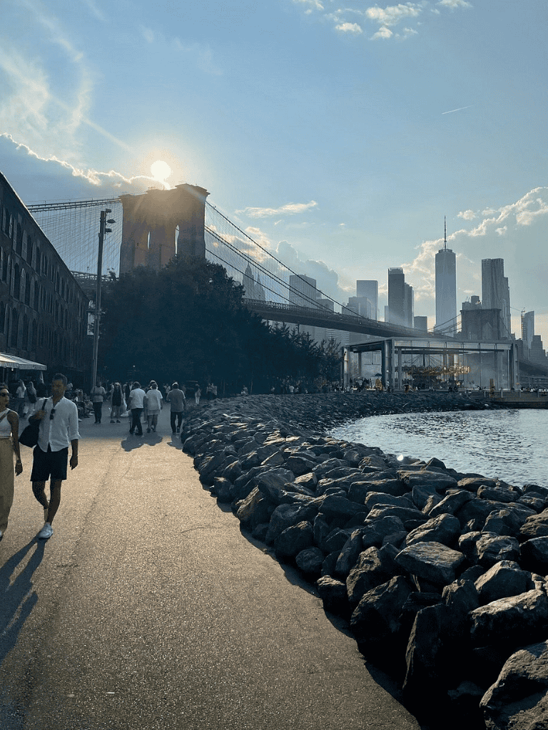 Brooklyn Bridge and Manhattan skyline in New York City at sunset, scenic waterfront view with pedestrians.