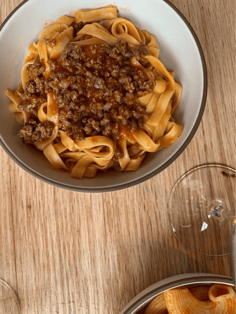 Hearty beef bolognese over fresh fettuccine pasta on a rustic wooden table.