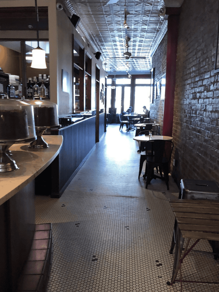 Cozy cafe interior with brick walls and large windows, perfect for relaxed dining or coffee breaks.