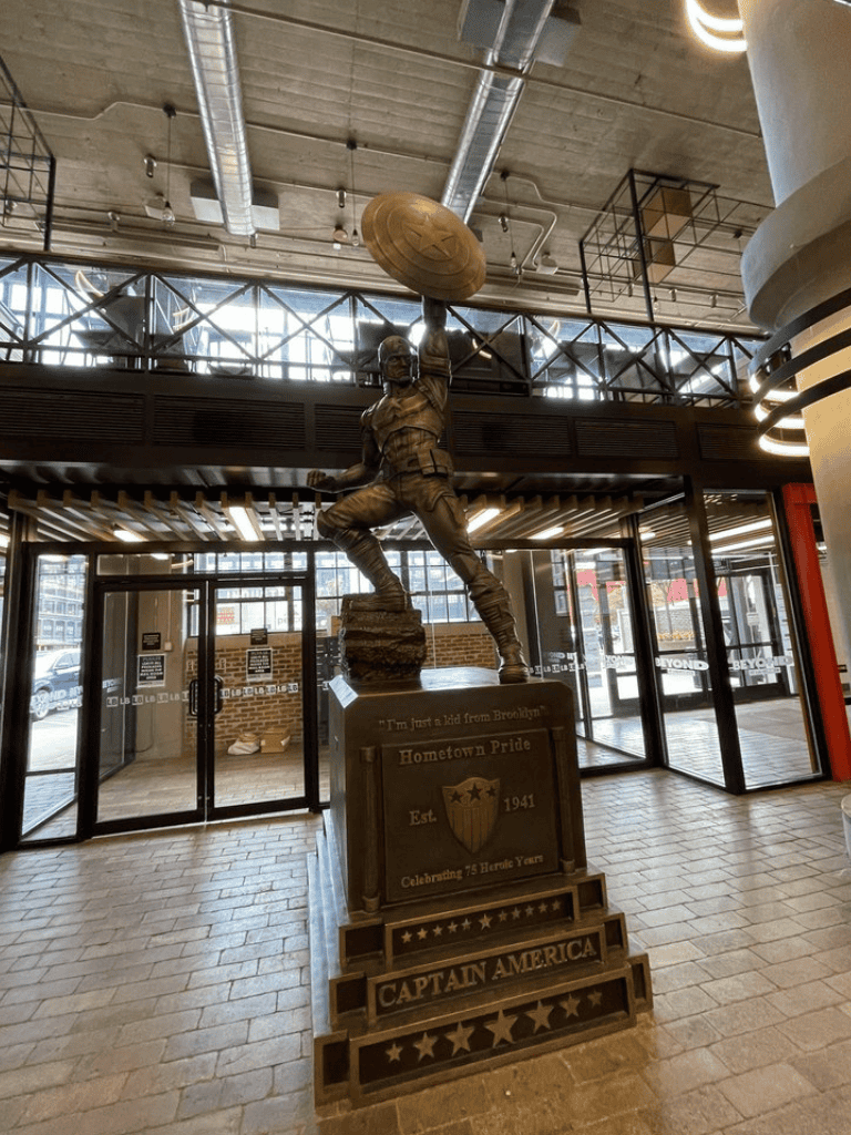 Heroic statue of Captain America holding his shield inside a modern building, celebrating heroic legacy and hometown pride.