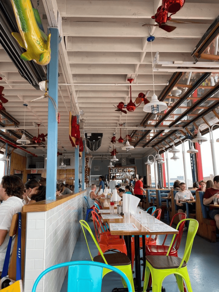 Brightly decorated, bustling restaurant interior with colorful chairs, hanging lights, and large windows at QuestForDirections.