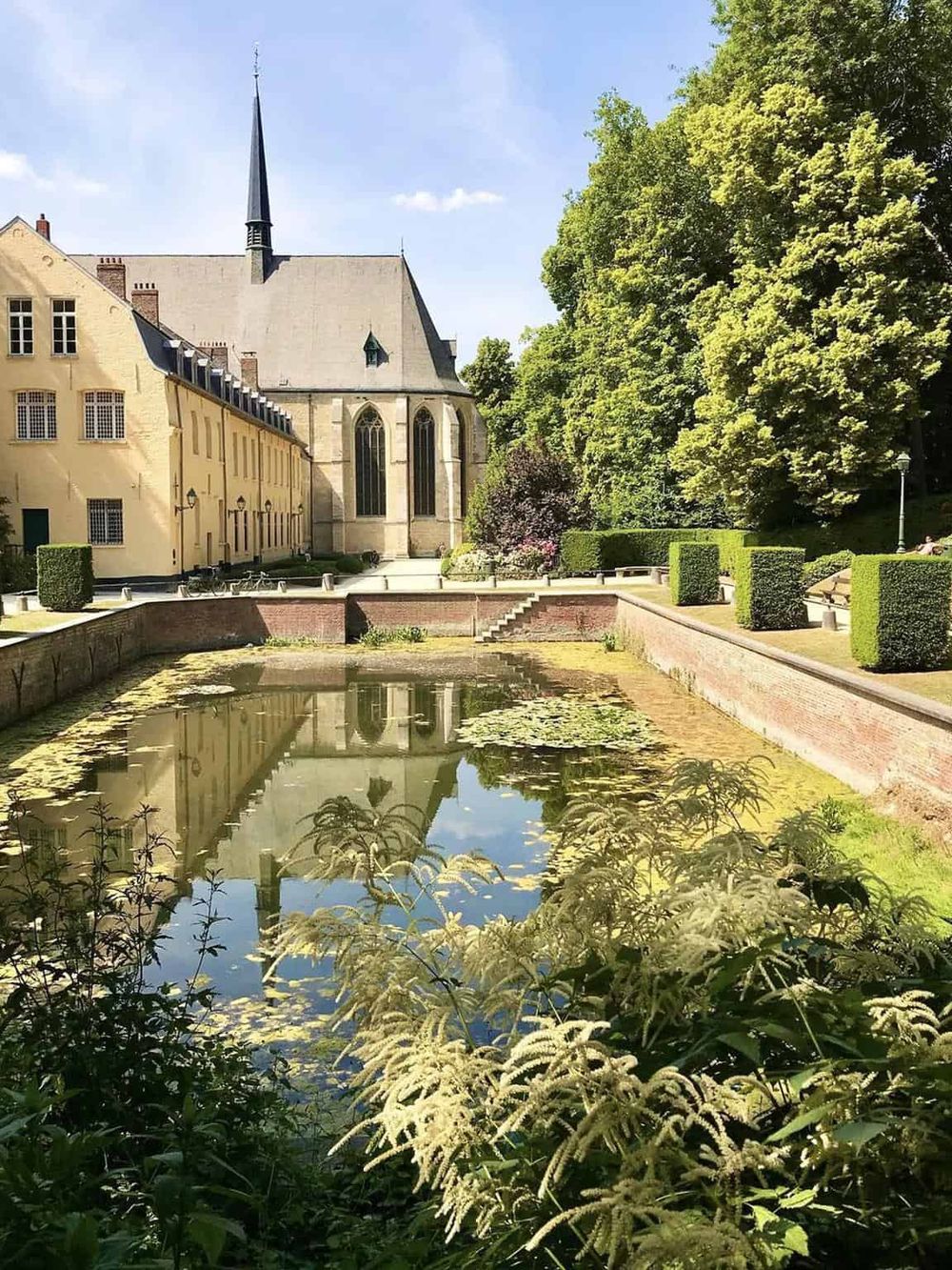 Serene historic church with lush green garden, pond, and bright sky in the background.
