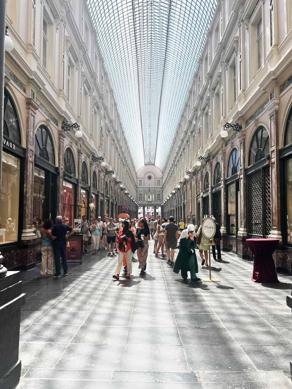 Elegant indoor shopping arcade with natural light and shoppers, historic architecture, high-end boutiques, and luxurious ambiance.