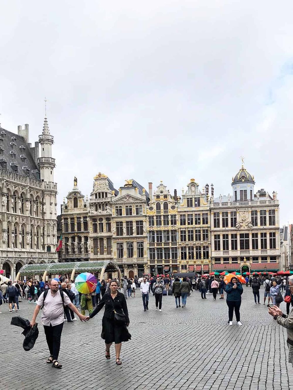 Colorful umbrellas in a bustling European city square, showcasing historic architecture and vibrant street life.