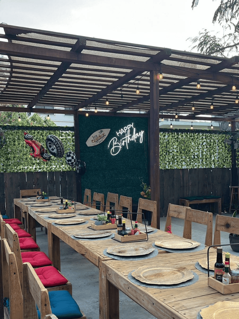 Happy Birthday outdoor celebration venue with decorated wooden table, neon sign, and racing car decor elements.