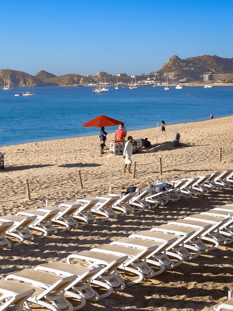 Relaxing beach scene with lounge chairs and sailing boats in the harbor, perfect for a seaside vacation.